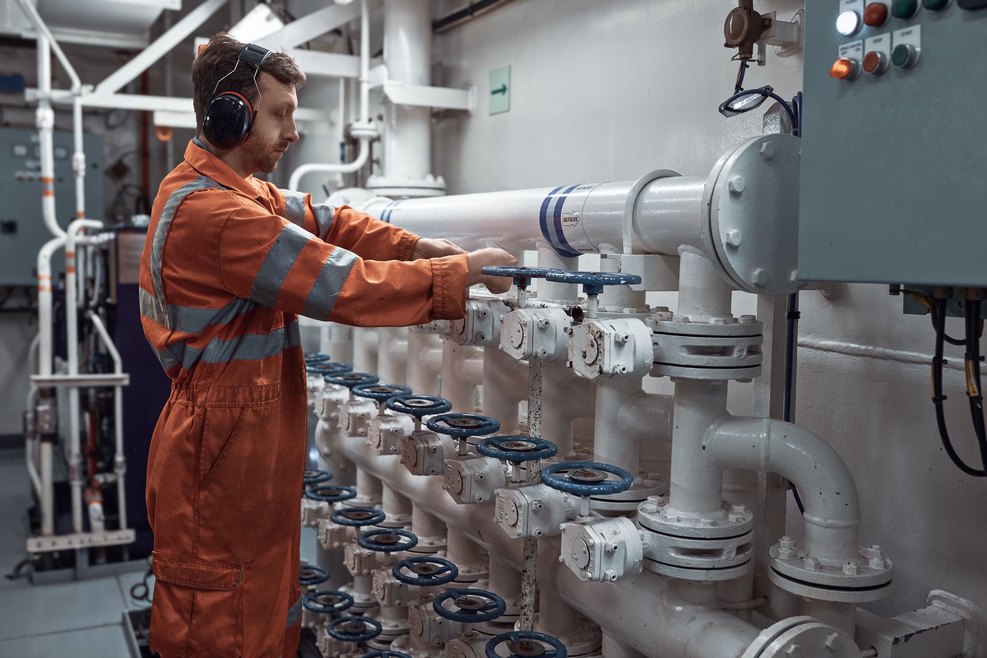 Marine engineer manually operating valve on valve manifold.